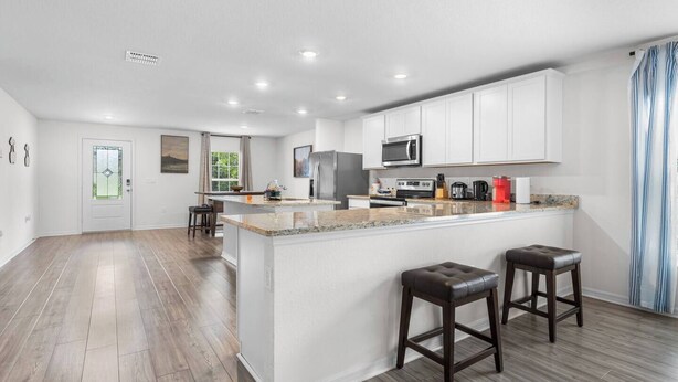 A modern kitchen with white cabinets, a granite countertop, stainless steel appliances, and a central island with stools.
