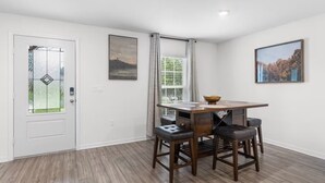 A dining area with a wooden table and four chairs, a glass door with a geometric pattern, and two framed pictures on the walls.