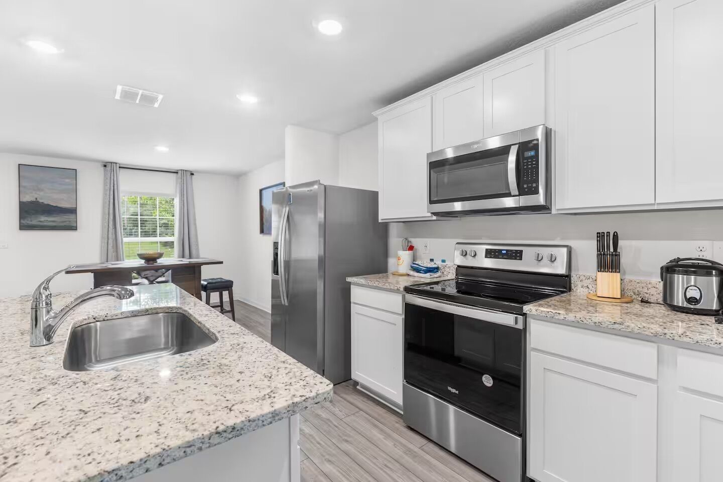 A modern kitchen with stainless steel appliances, a granite countertop, and white cabinetry.
