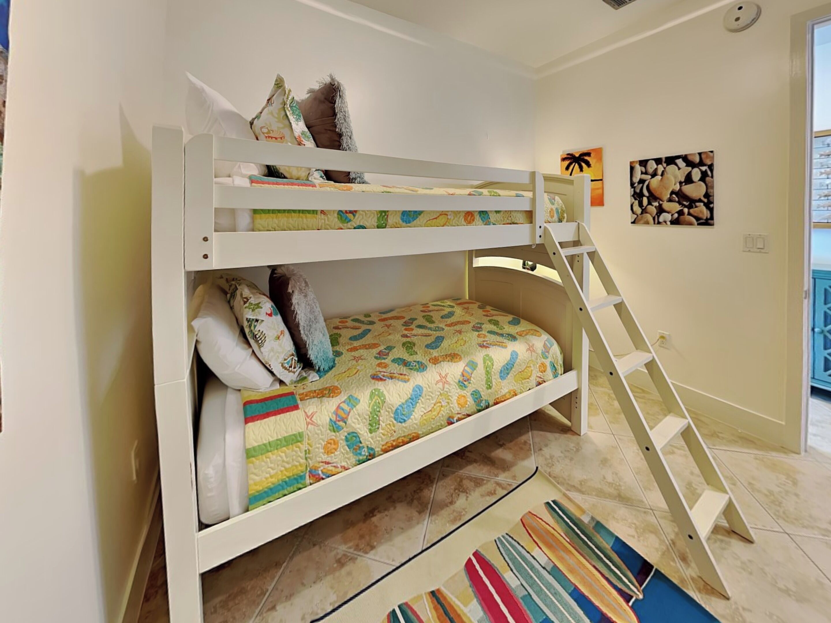 A bunk bed with a ladder, colorful bedding, and pillows. There are two wall art pieces and a window with a view.