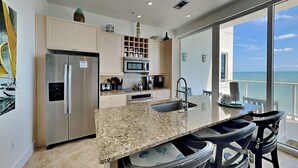 A modern kitchen with granite countertops, stainless steel appliances, and a large island with bar stools. - Tranquility Beach | Oceanfront Condo (Galveston)