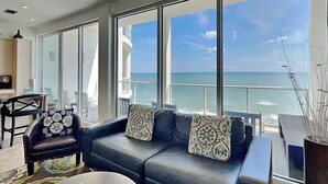 A modern living room with a leather sofa, a coffee table, and a view of the ocean. - Tranquility Beach | Oceanfront Condo (Galveston)