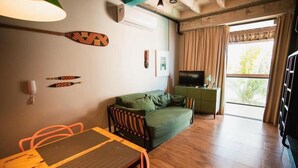 Une pièce avec un canapé vert, une table à manger en bois et un téléviseur posé sur un meuble vert.