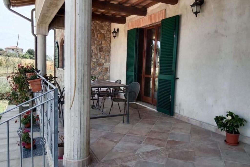 A covered outdoor patio with a table and chairs, stone walls, and green shutters.