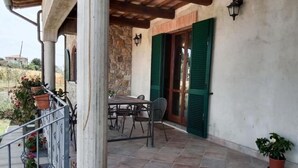 Eine überdachte Terrasse im Freien mit Tisch und Stühlen, Steinmauern und grünen Fensterläden.