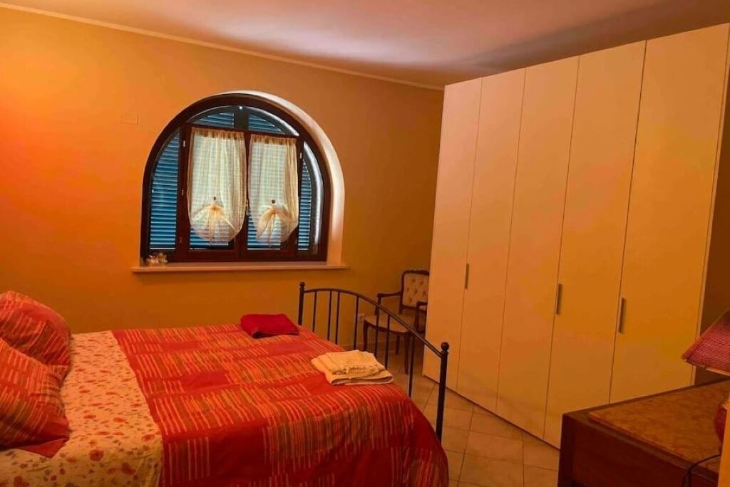 A bedroom with a bed, a window with curtains, a wardrobe, and a chair.