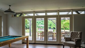 Ein Zimmer mit Billardtisch, einem gemütlichen Sessel und großen Schiebeglastüren, die zu einer Außenpatiofläche führen.