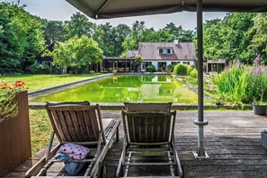 A wooden deck with two lounge chairs facing a pond and a house in the background. - Attractive villa in the middle of the forest, pet-friendly with swimming pond (Ede)