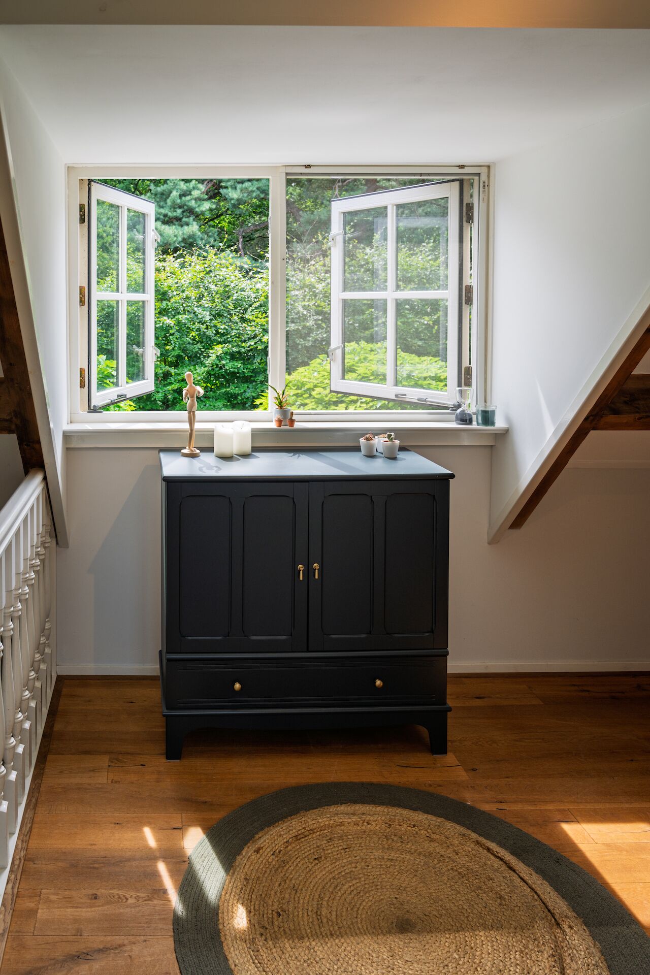 A room with a dark wooden cabinet, a window with an open shutter, and a view of greenery outside.
