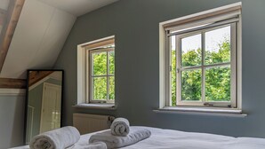 Ein Schlafzimmer mit einem Bett, zwei Fenstern, einem Heizkörper und einem Spiegel.