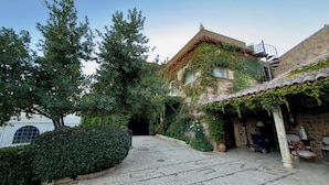 A courtyard with a stone building, a large tree, and a neatly trimmed hedge. - PALACIO ARUDECAS (Cañada de Calatrava)