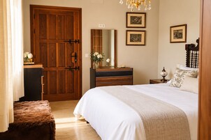 A bedroom with a wooden wardrobe, a dresser, a bed with white bedding, a mirror, and framed pictures on the wall.