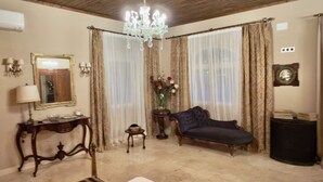 A room with a chandelier, a sofa, a side table, a mirror, and curtains. - PALACIO ARUDECAS (Cañada de Calatrava)