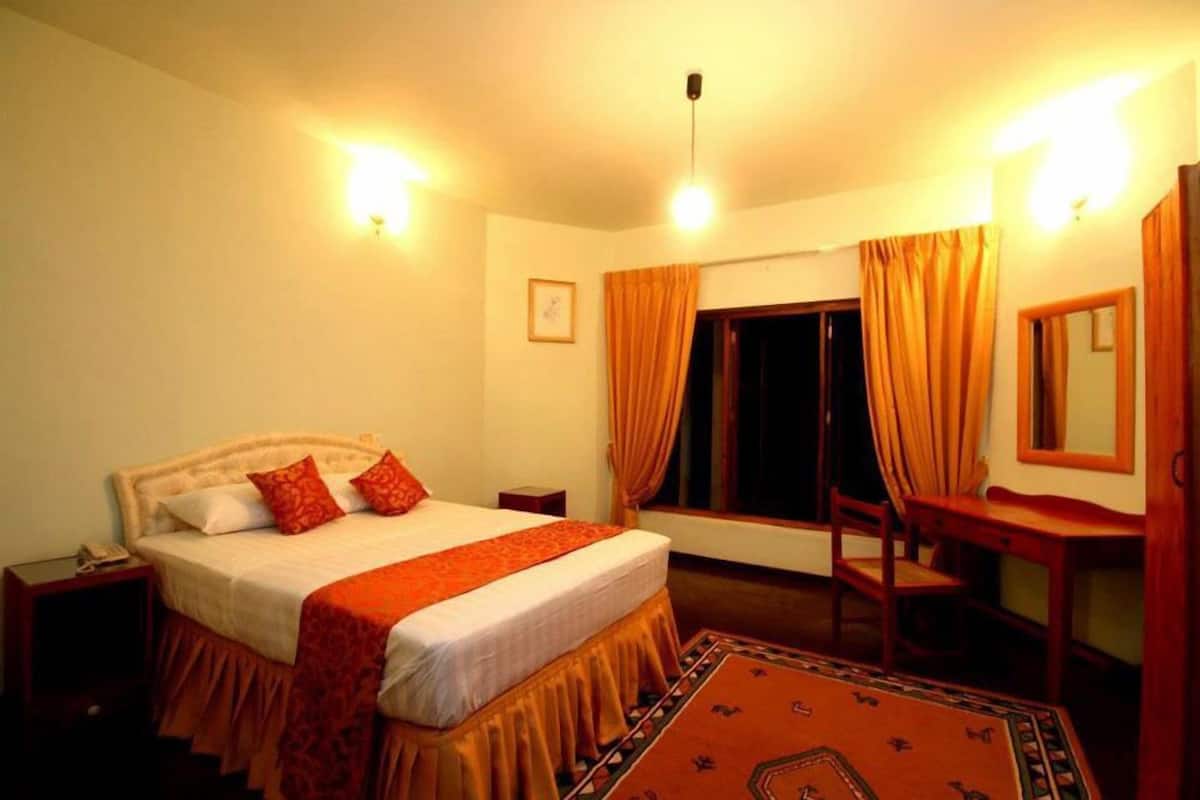 Una habitación de hotel con cama, mesita de noche, silla, escritorio y un ventanal con cortinas.