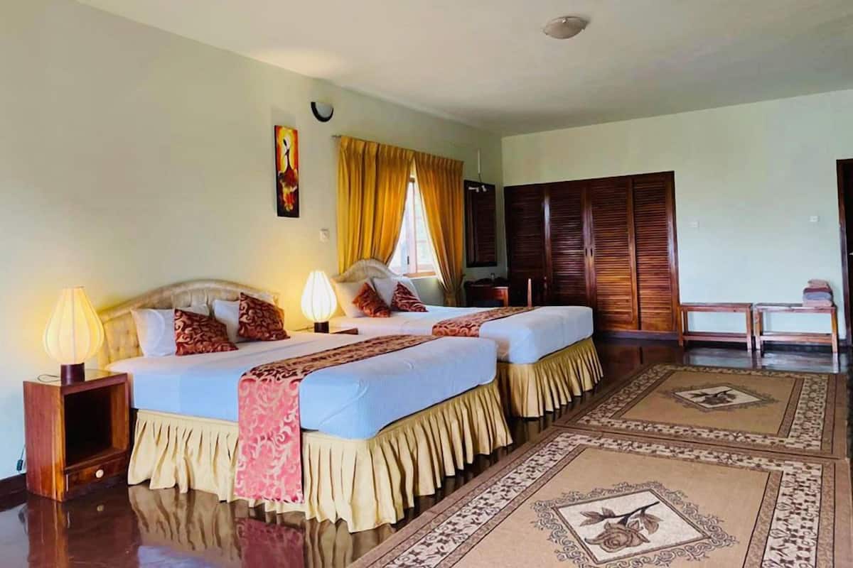 Una habitación de hotel con dos camas, un armario de madera, una mesita pequeña y una mesita de noche con lámpara.