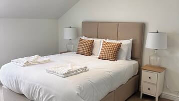 A neatly made bed with white linens and patterned pillows, a bedside table with a lamp, and a carpeted floor.
