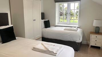 A bedroom with two beds, a wardrobe, a window with a view, and a bedside table with a lamp.