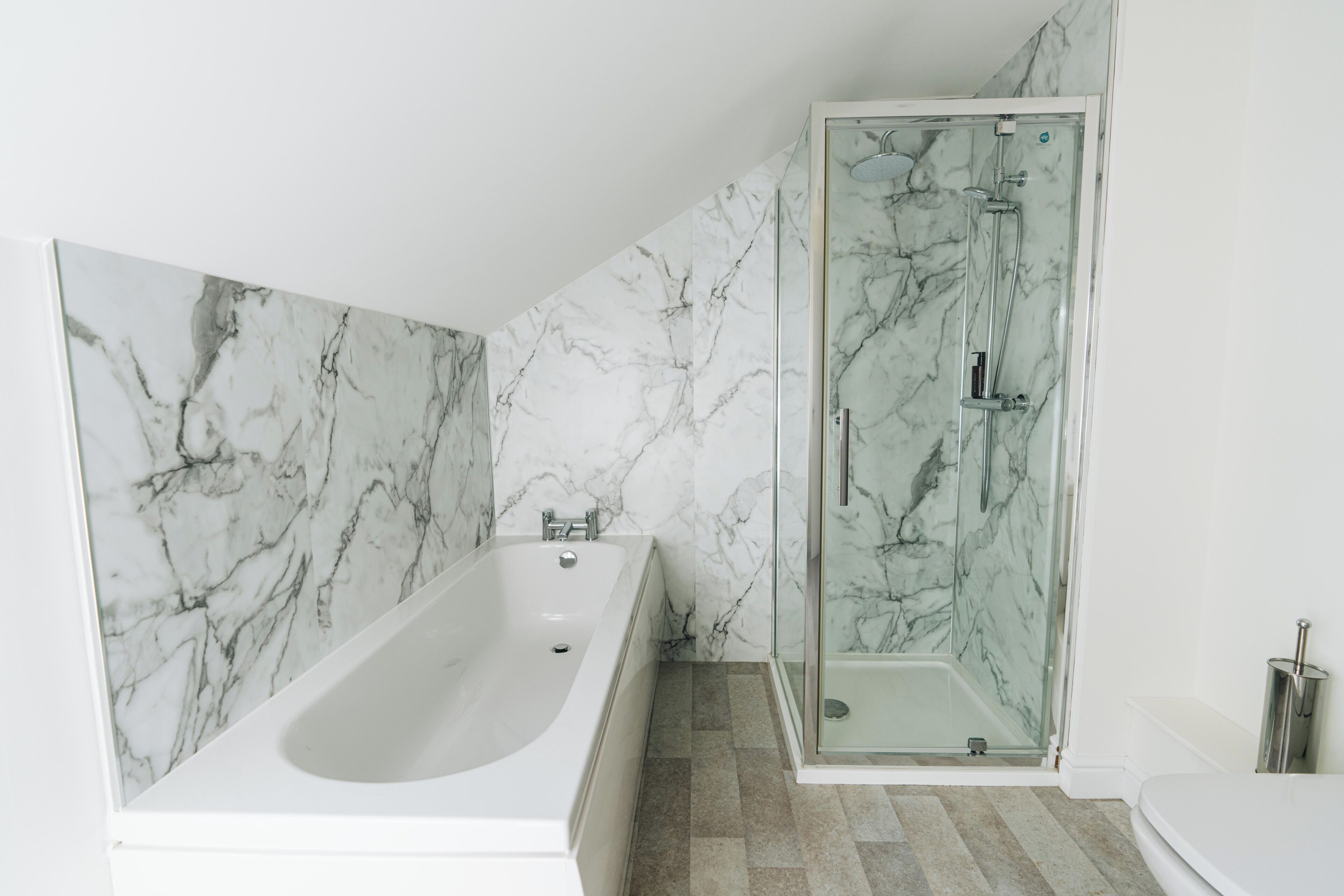 A bathroom with a marble wall, a bathtub, and a glass-enclosed shower.