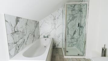 A bathroom with a marble wall, a bathtub, and a glass-enclosed shower.