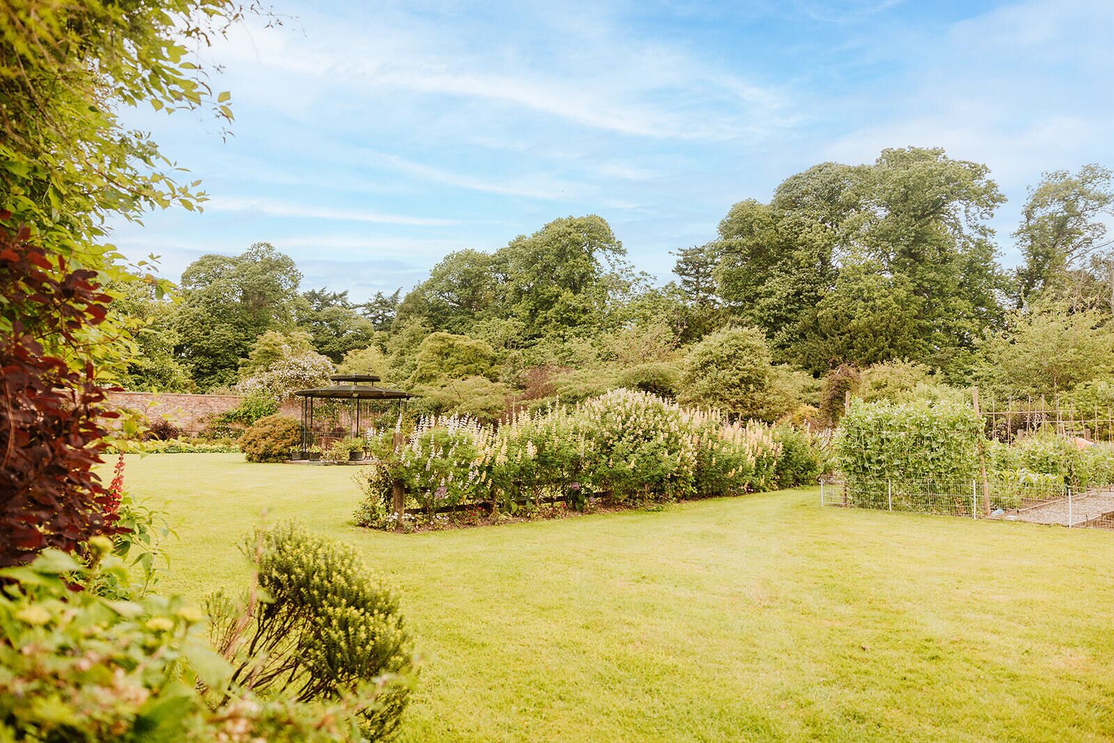 A well-maintained garden with a gazebo, various plants, and trees.