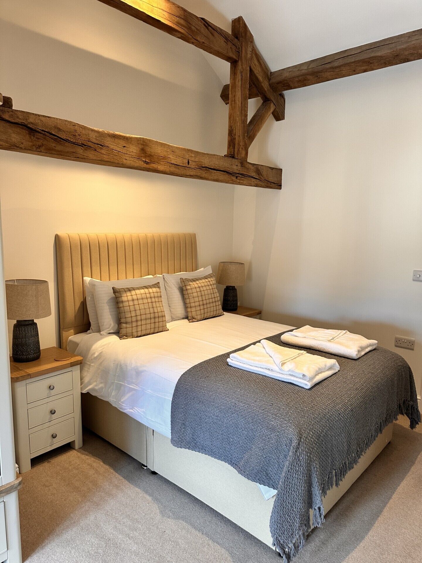 A bedroom with a bed, nightstands, and a wooden ceiling beam.
