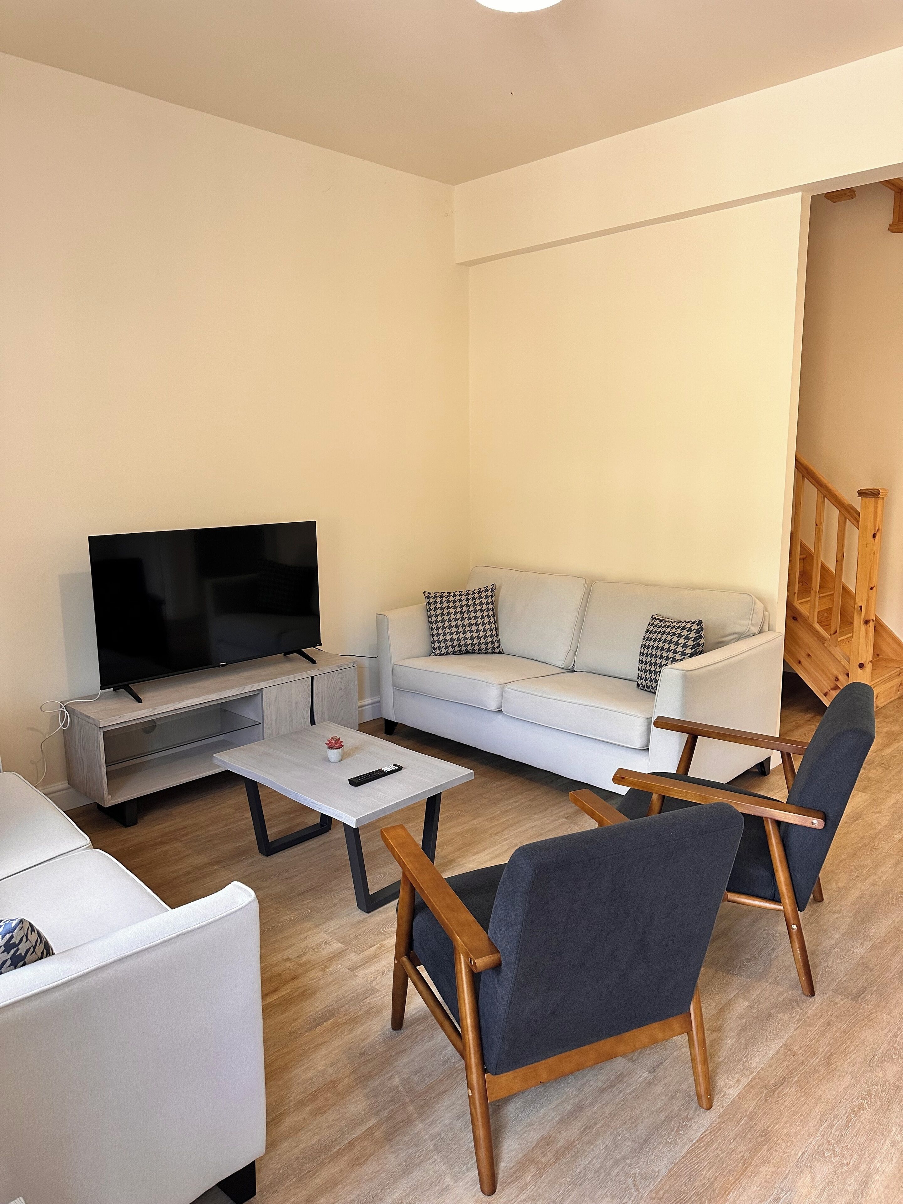 A modern living room with a flat-screen TV, a white sofa, two armchairs, and a coffee table.