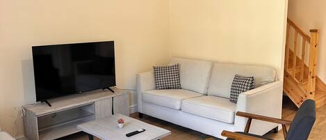 A modern living room with a flat-screen TV, a white sofa, two armchairs, and a coffee table.