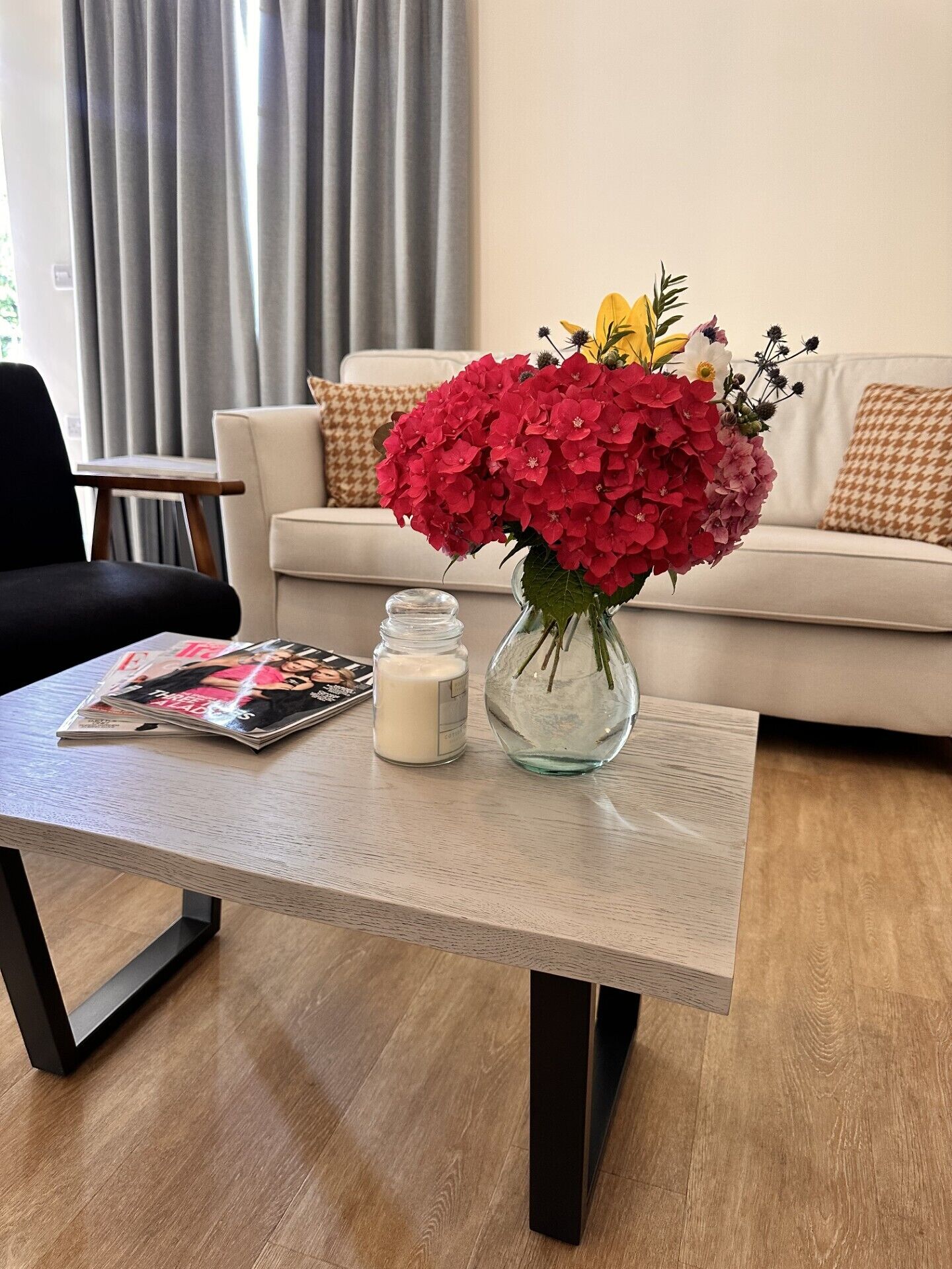 Ein Wohnzimmer mit einer Couch, einem Couchtisch mit Blumenvase, einer Kerze und einer Zeitschrift.
