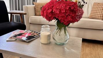 Ein Wohnzimmer mit einer Couch, einem Couchtisch mit Blumenvase, einer Kerze und einer Zeitschrift.