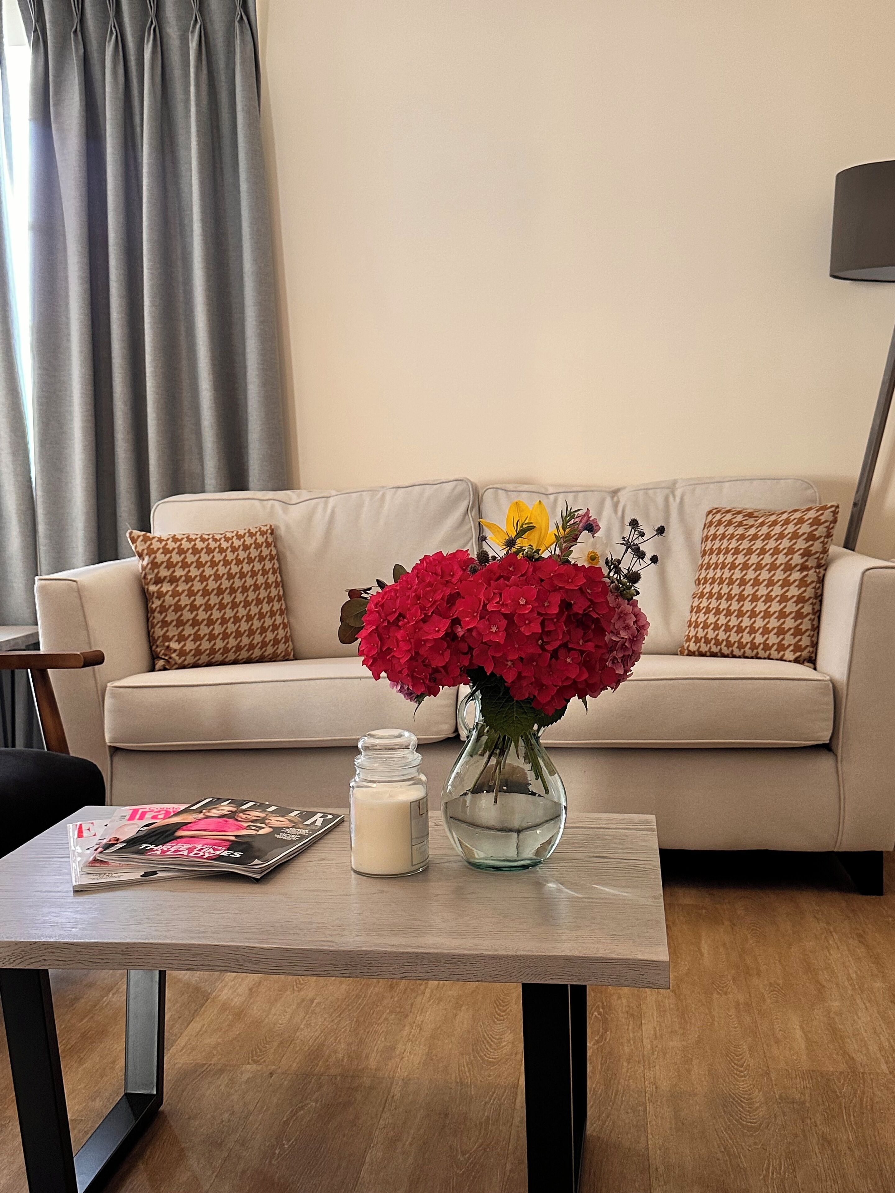 A living room with a sofa, a coffee table, a vase with flowers, a candle, and a magazine.