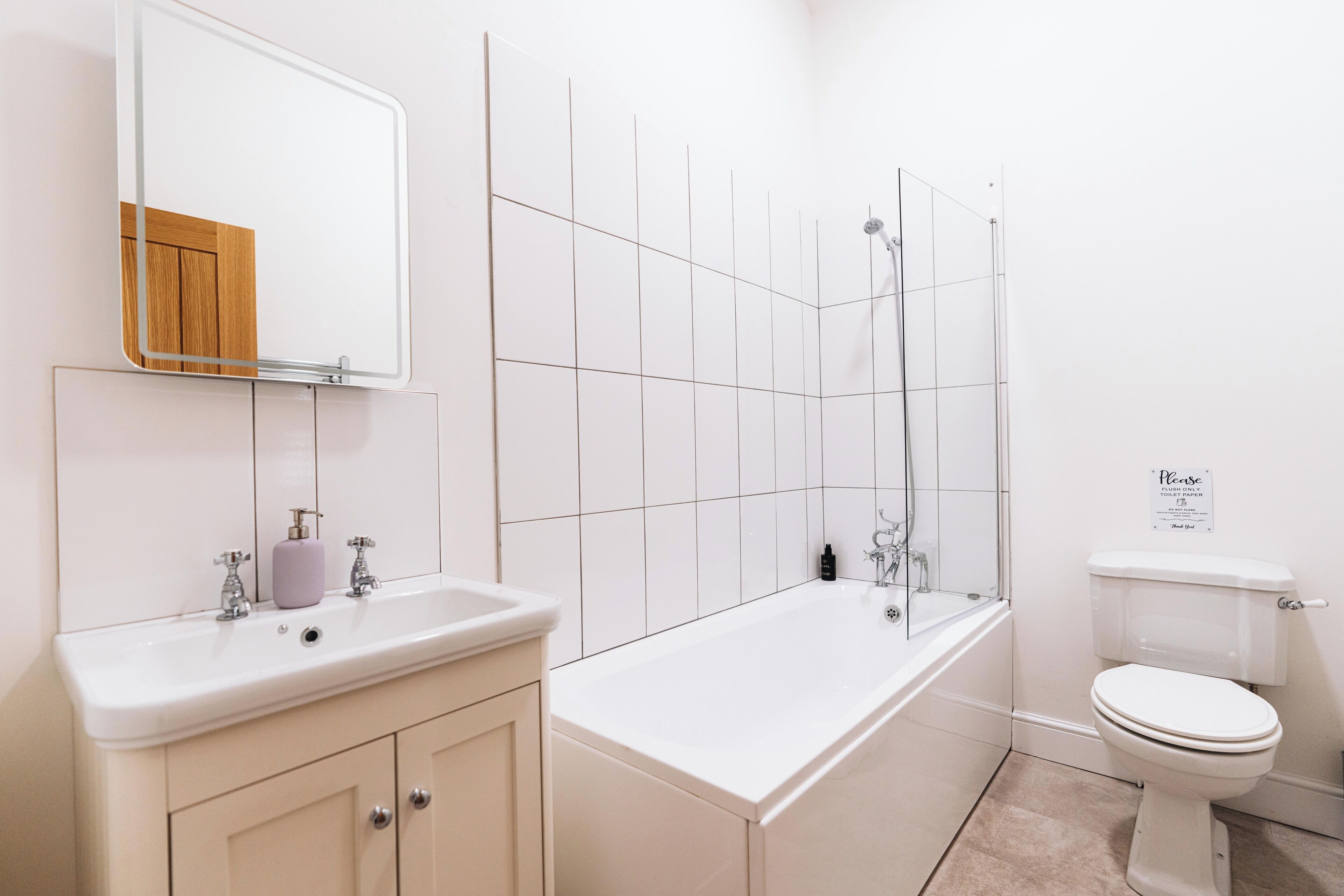 A modern bathroom with a white sink, vanity, bathtub, and toilet.