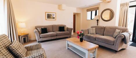 A living room with two sofas, a coffee table, and a chair. There is a picture on the wall, a lamp, and a mirror.