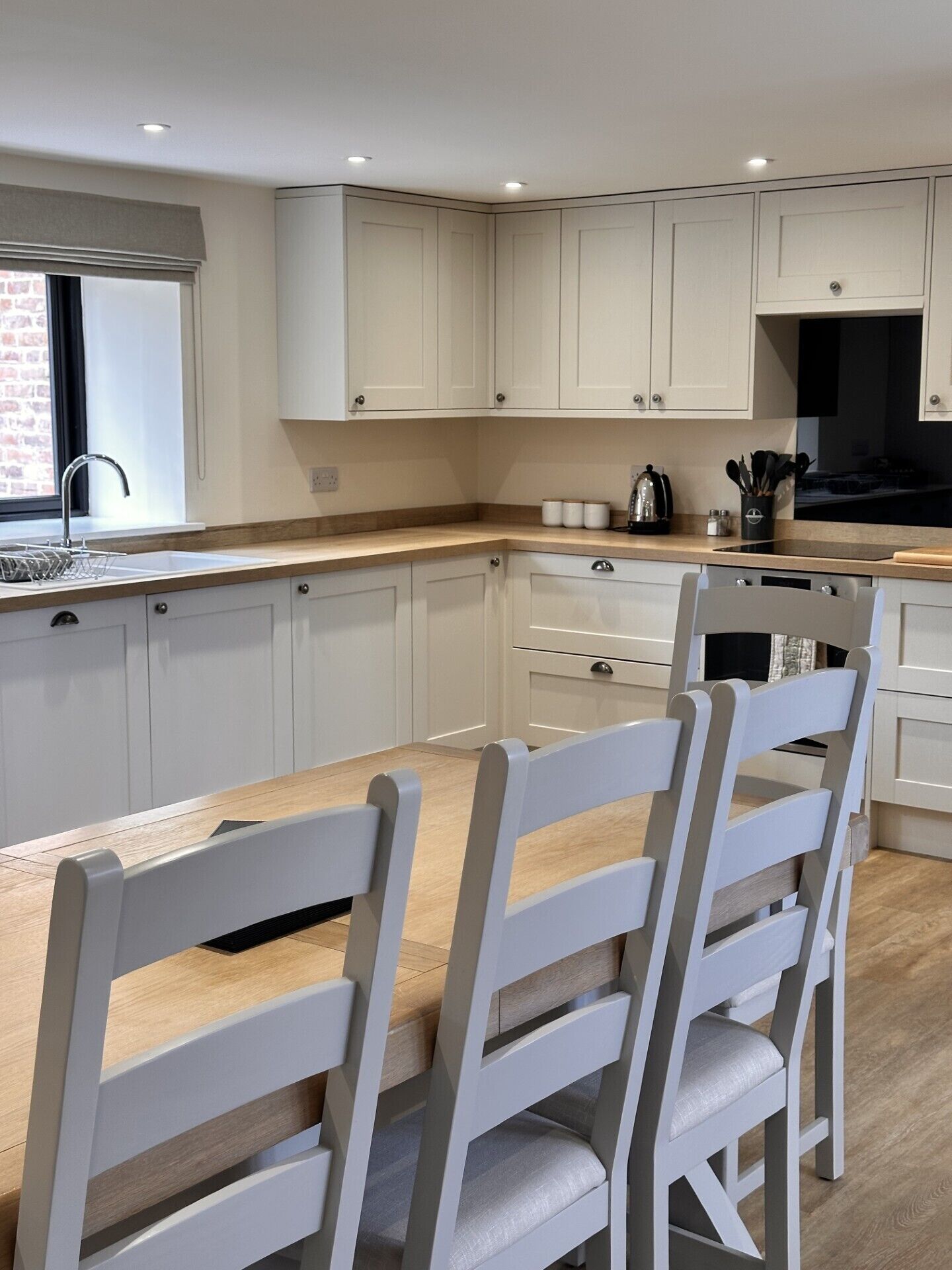 Een moderne keuken met witte kasten, een houten aanrecht en een eethoek met witte stoelen.