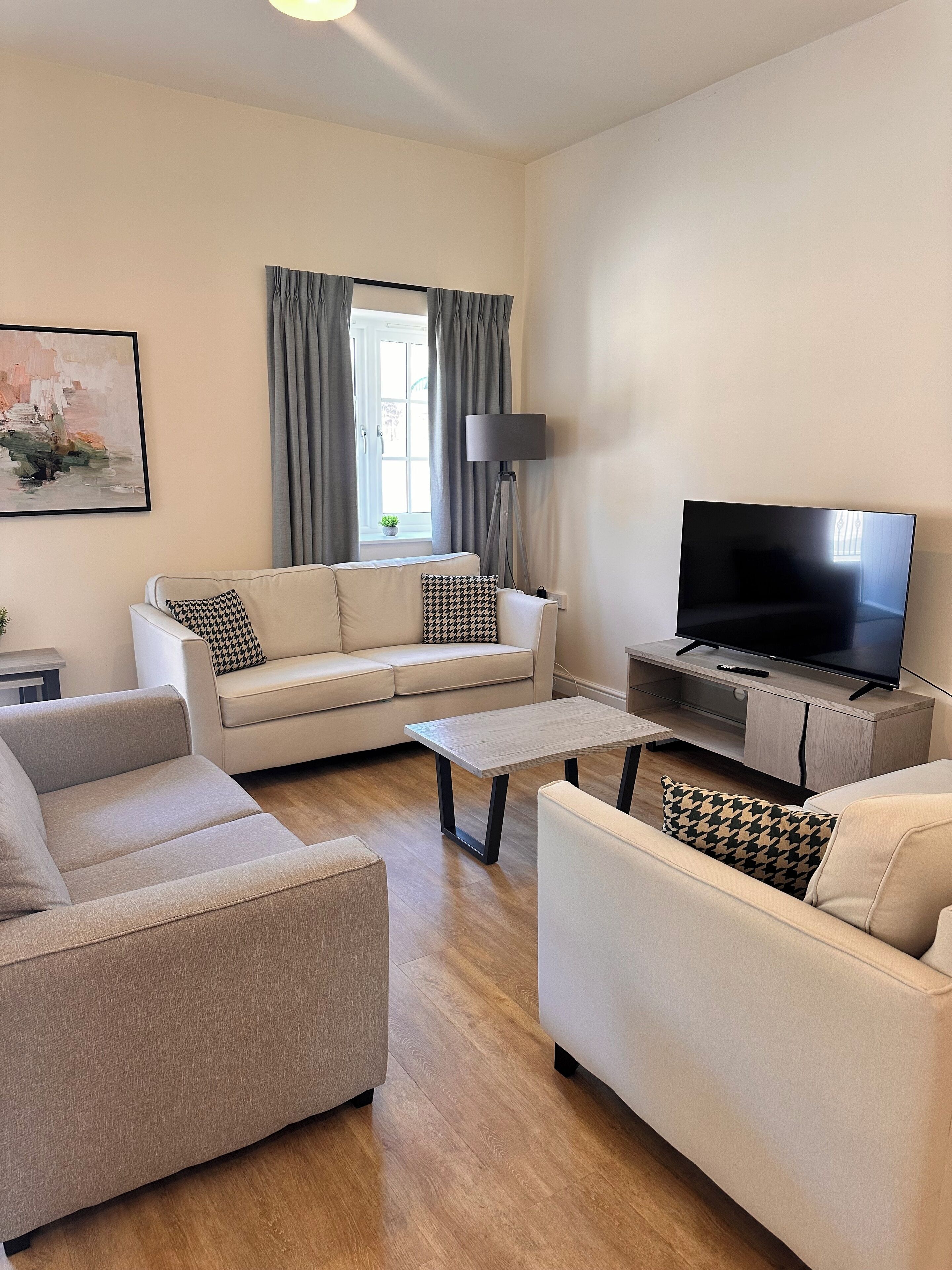 Una sala de estar moderna con un sofá, dos sillones, una mesa de centro, un televisor y una lámpara de pie.