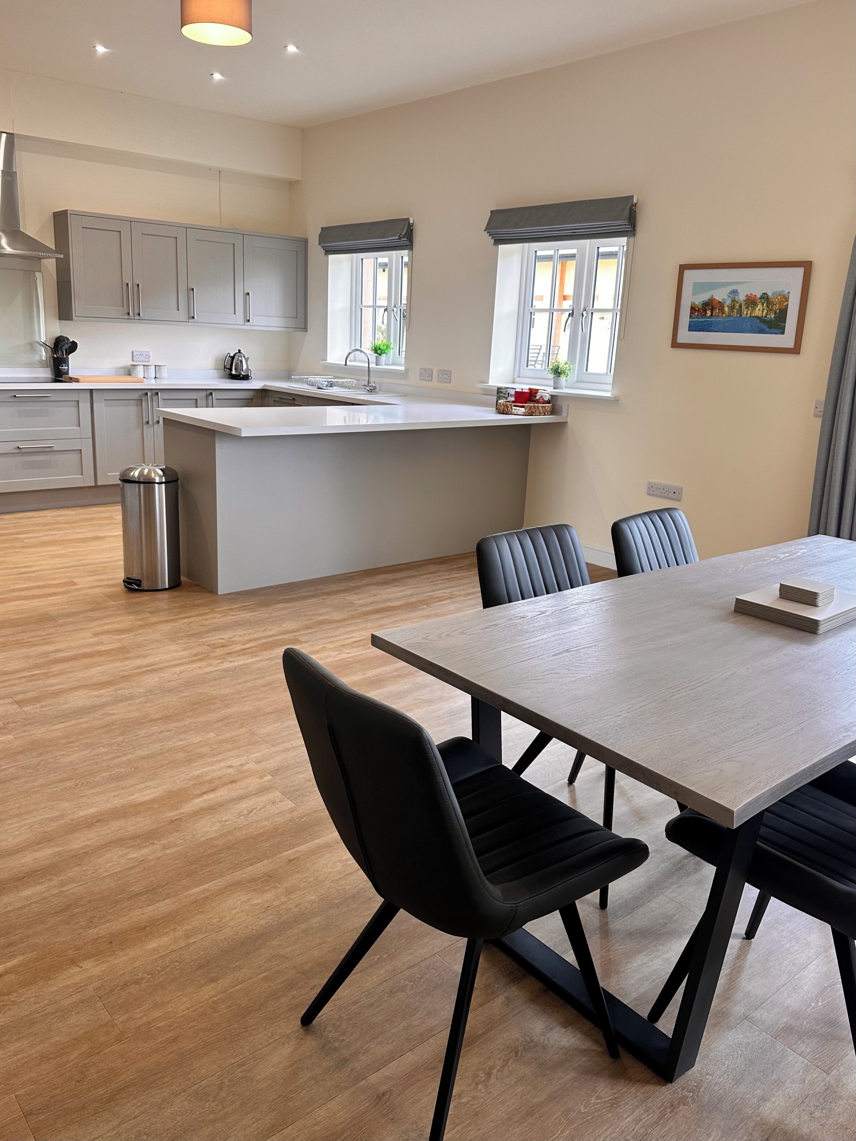 A modern kitchen with grey cabinets, a central island, and a dining area with a table and chairs.