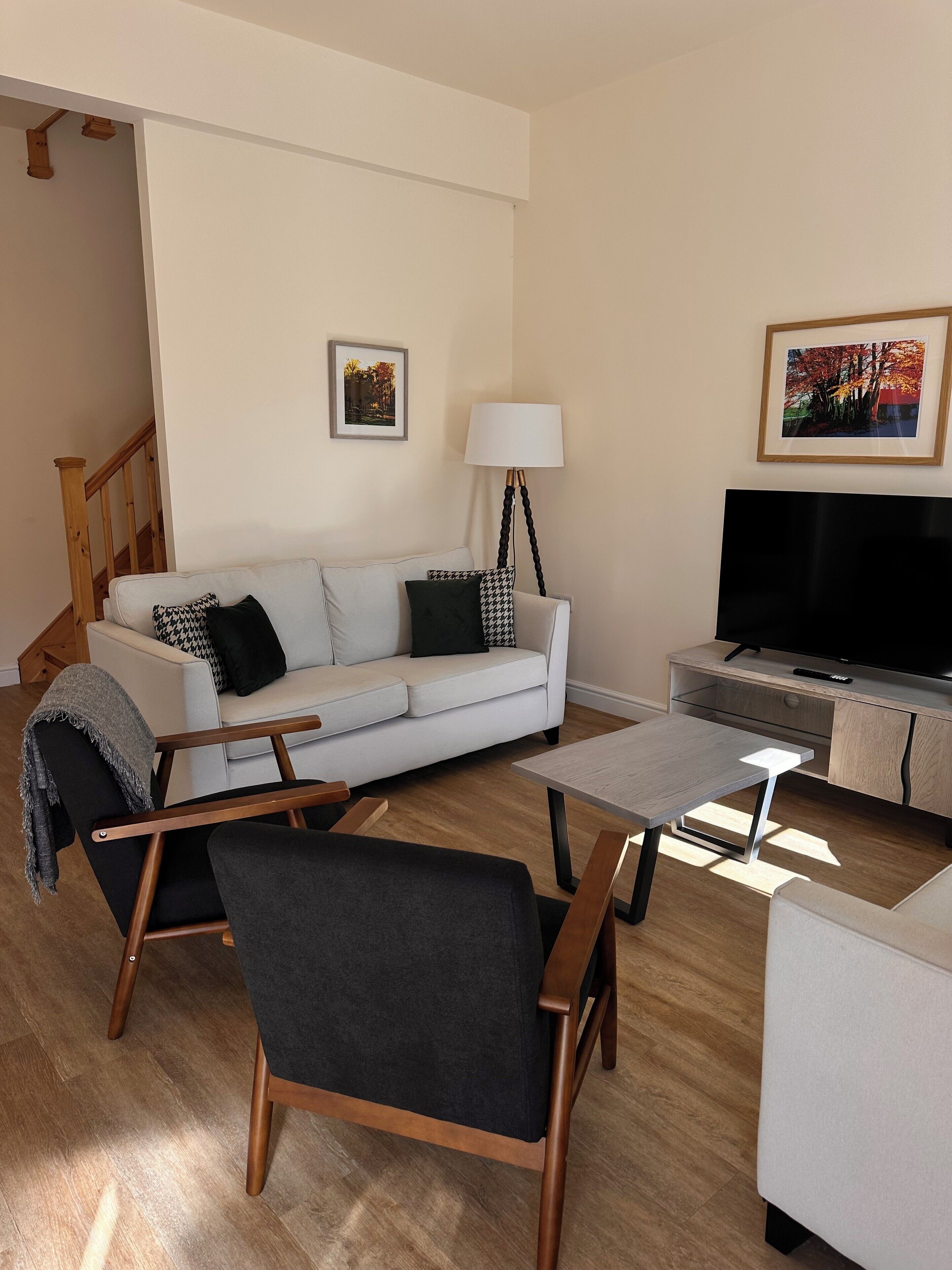 A living room with a white sofa, a black armchair, a coffee table, a TV stand, and a lamp.