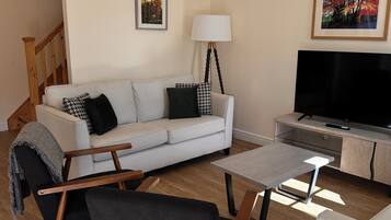 A living room with a white sofa, a black armchair, a coffee table, a TV stand, and a lamp.