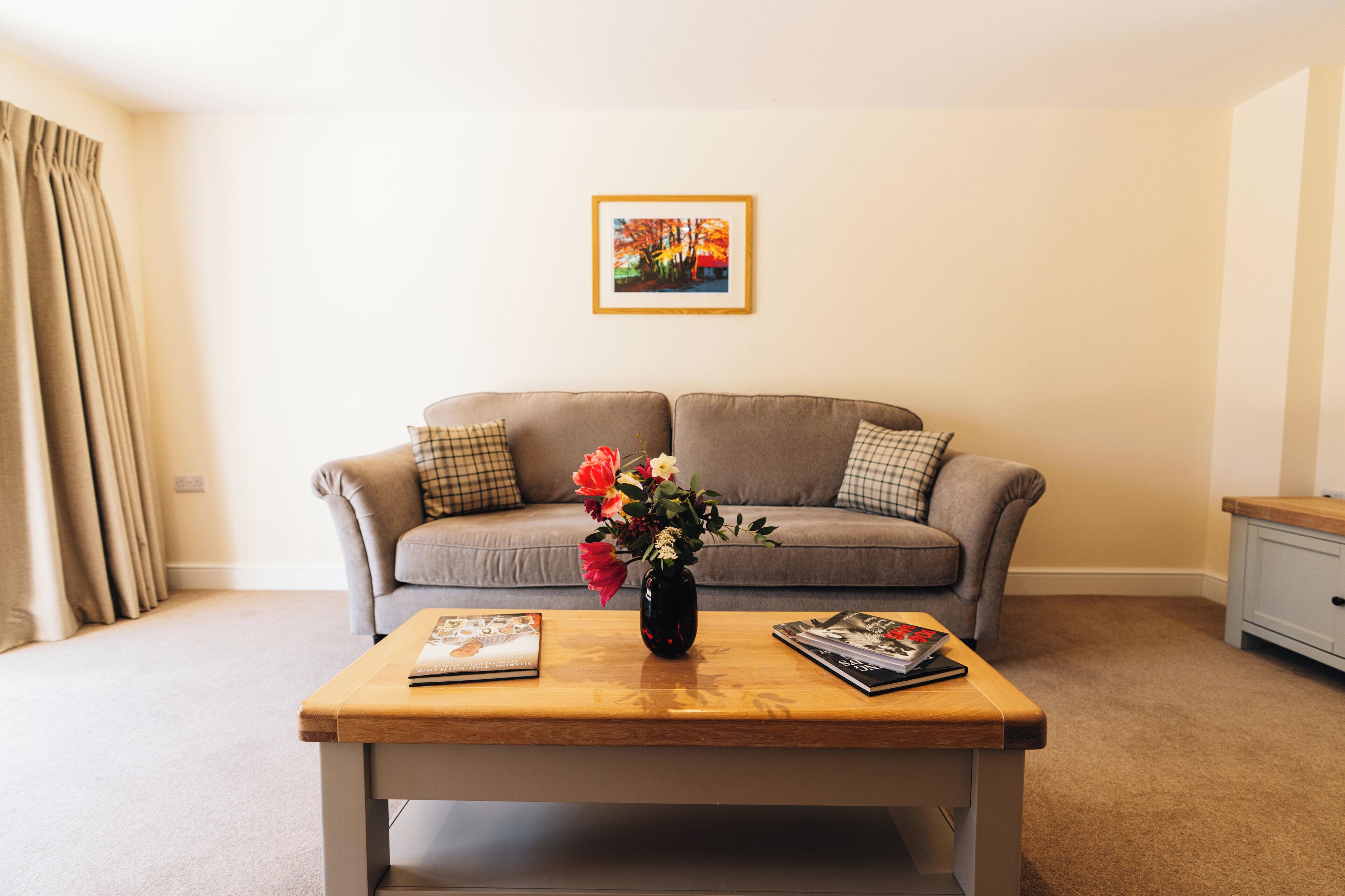 A living room with a sofa, a coffee table with a vase of flowers, and a framed picture on the wall.