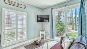 A living room with a TV, a coffee table with a decorative bowl, a couch with pillows, and a sign that reads "BEACH HOUSE". - Adorable Upstairs 2 BR Nantucket 6AB (Destin)