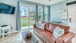 A living room with a brown leather sofa, a flat-screen TV, and a coffee table with decorative items. - Adorable Upstairs 2 BR Nantucket 6AB (Destin)