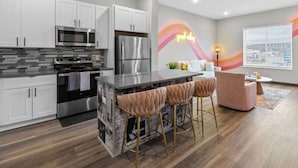 A modern kitchen with white cabinets, stainless steel appliances, and a bar area with cushioned stools.