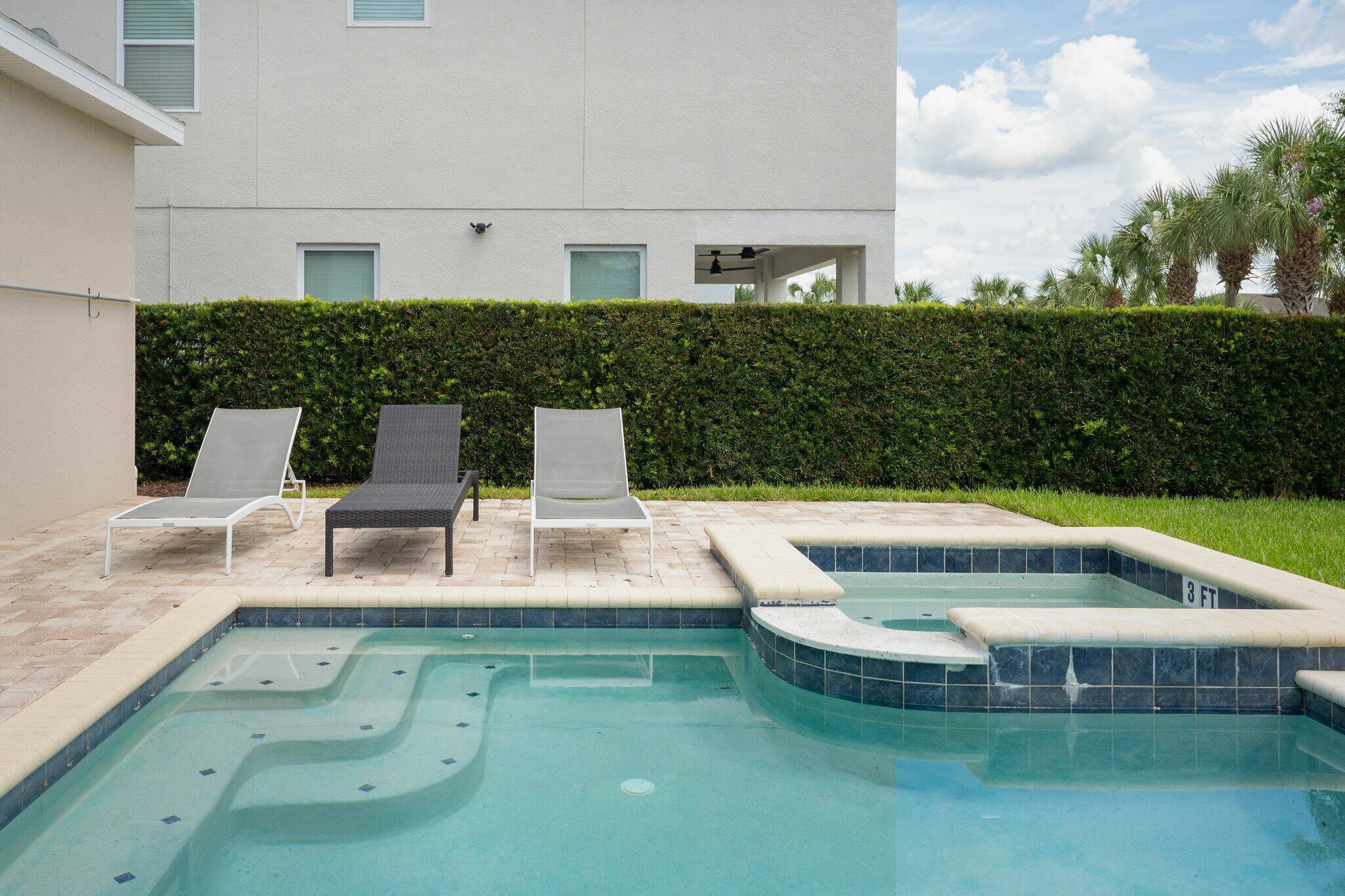 A swimming pool with two lounge chairs and a small hot tub.