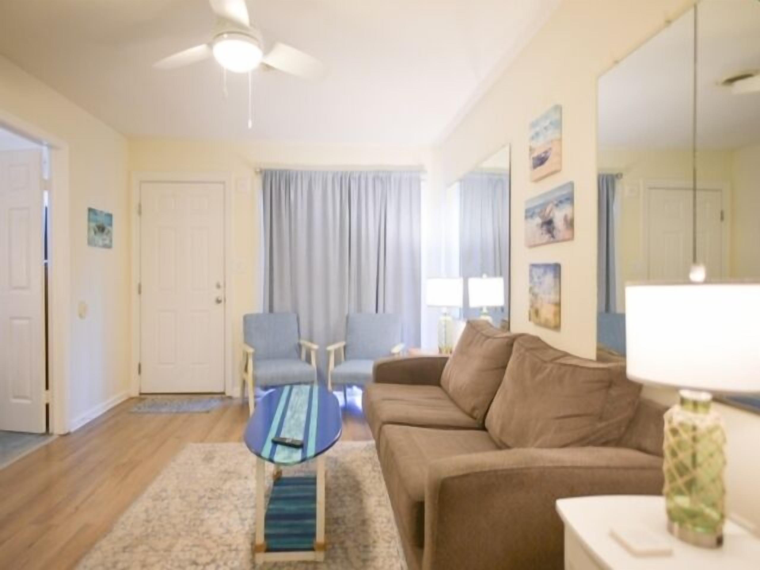 A living room with a ceiling fan, a sofa, two armchairs, a coffee table, and a lamp.