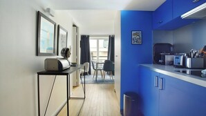 Una cucina moderna con mobili blu, un'area pranzo con tavolo e sedie, e un corridoio che conduce a un balcone.