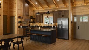 A modern kitchen with wooden walls, a central island with bar stools, stainless steel appliances, and pendant lighting. - New 4-King Cabin w/ Cave View, Hot Tub, Fire Pit (Frenchburg)