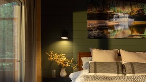 A bedroom with a large bed, a bedside table with a vase of flowers, and a painting of a waterfall on the wall. - New 4-King Cabin w/ Cave View, Hot Tub, Fire Pit (Frenchburg)