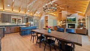 A spacious kitchen with wooden cabinets, a large island, and a dining area with a long table and chairs. - New 4-King Cabin w/ Cave View, Hot Tub, Fire Pit (Frenchburg)