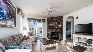 A living room with a sofa, coffee table, TV, fireplace, and a large painting. - Dog‑Friendly (Only 1) Bayside Condo w/ Pool & Gym (Selbyville)