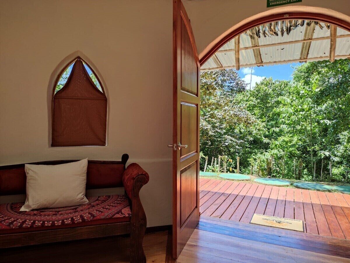 Ein Zimmer mit einer Holzbänklage und einem Fenster, das auf eine Außenterrasse mit Blick auf Bäume führt.