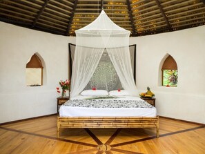 A bed with a canopy, a small table with a vase of flowers, and two windows with plants.